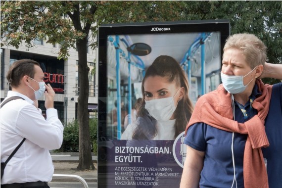 Warga menunggu trem di depan sebuah poster yang mengingatkan masyarakat untuk mengenakan masker di Budapest, Hongaria, pada 23 September 2020. (Xinhua/Attila Volgyi)