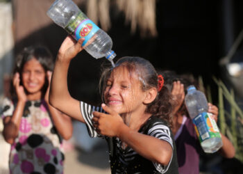 Seorang anak perempuan Palestina menyiram air ke tubuhnya untuk mendinginkan diri saat cuaca panas di dekat kamp pengungsi Khan Younis di Jalur Gaza selatan pada 29 Juni 2021. (Xinhua)