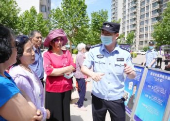 Foto yang diabadikan pada 3 Juni 2021 ini menunjukkan seorang petugas polisi berbagi informasi tentang cara mengidentifikasi dan mencegah tindak penipuan telekomunikasi dan internet kepada warga setempat di sebuah permukiman di Kota Shijiazhuang, Provinsi Hebei, China utara. (Xinhua/Yang Shiyao)