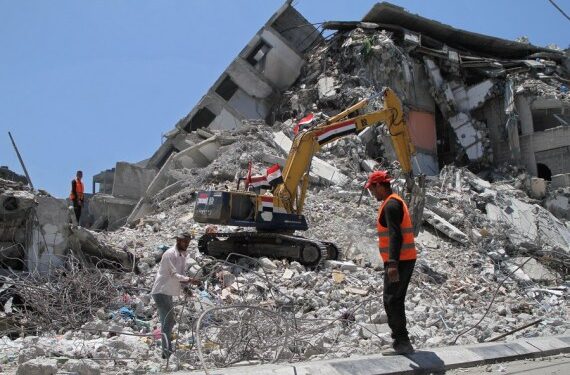 Sejumlah pekerja Palestina dan sebuah buldoser dari Mesir terlihat memindahkan reruntuhan bangunan yang hancur akibat serangan udara Israel bulan lalu di Gaza City pada 6 Juni 2021. (Xinhua/Rizek Abdeljawad)