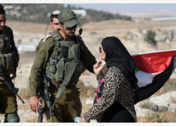 Seorang wanita Palestina berbicara dengan tentara Israel dalam aksi massa march yang digelar oleh pemukim Israel di Desa Yatta, sebelah selatan Kota Hebron, Tepi Barat, pada 21 Juni 2021. (Xinhua/Mamoun Wazwaz)