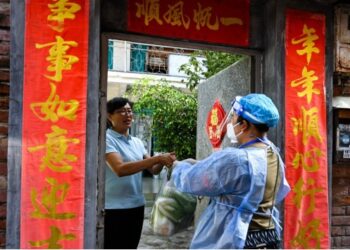 Seorang petugas perangkat jaringan masyarakat mengantar kebutuhan sehari-hari ke sebuah rumah yang sedang dikarantina di Kota Ruili, Provinsi Yunnan, China barat daya, pada 8 Juli 2021. (Xinhua/Wang Guansen)