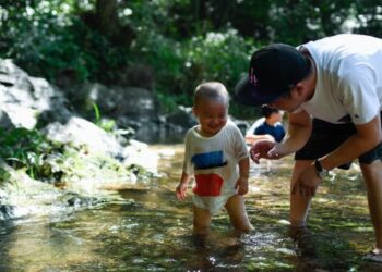 Seorang ayah bersama anaknya merendam kaki di dalam sungai untuk menyejukkan diri di objek wisata Jiuxi di Hangzhou, Provinsi Zhejiang, China timur, pada 3 Agustus 2020. (Xinhua/Huang Zongzhi)