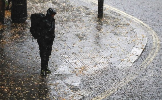 Seorang pria berdiri di pinggir jalan saat hujan lebat di London, Inggris, pada 25 Juli 2021. (Xinhua/Han Yan)