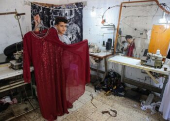 Bocah laki-laki Palestina Ahmed Abbas menunjukkan gaun yang dia rancang di tempat menjahit milik keluarganya di kamp pengungsi Shati di Gaza City pada 11 Juli 2021. (Xinhua/Rizek Abdeljawad)