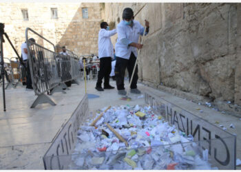 Para pekerja membersihkan Tembok Ratapan dari kertas-kertas catatan yang ditulis dengan tangan dan diselipkan di antara bebatuan kuno tersebut di Kota Tua Yerusalem pada 25 Agustus 2021. (Xinhua/Muammar Awad)