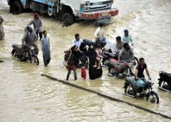 Orang-orang melewati sebuah jalan yang terendam banjir pascahujan lebat di kota pelabuhan Karachi di Pakistan selatan pada 23 September 2021. (Xinhua/Str)