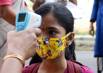 Seorang guru memeriksa suhu tubuh siswa di sebuah sekolah di Bangalore, India, pada 25 Oktober 2021. (Xinhua/Str)