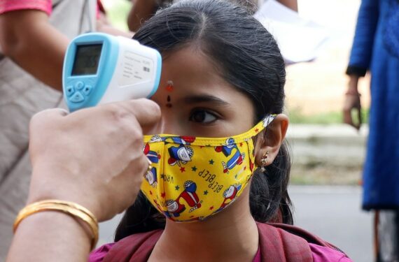Seorang guru memeriksa suhu tubuh siswa di sebuah sekolah di Bangalore, India, pada 25 Oktober 2021. (Xinhua/Str)