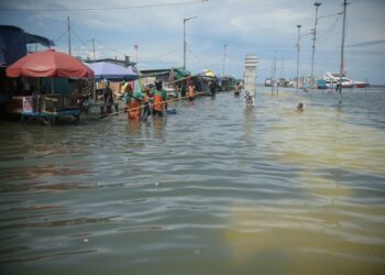 Orang-orang berjalan melintasi banjir di sebuah pelabuhan di kawasan pesisir Jakarta pada 9 November 2021. (Xinhua/Zulkarnain)