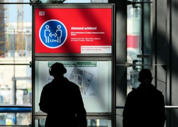 Dua pejalan kaki berdiri di dekat papan informasi yang mengingatkan orang-orang untuk menjaga jarak di Stasiun Kereta Pusat Berlin di Berlin, ibu kota Jerman, pada 16 April 2021. (Xinhua/Stefan Zeitz)