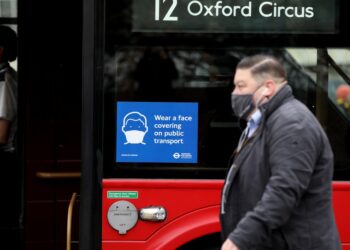 Seorang pria yang mengenakan masker berjalan melewati sebuah bus di London, Inggris, pada 24 November 2021. (Xinhua/Li Ying)