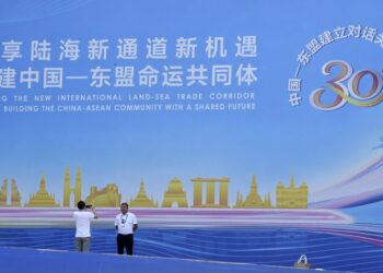 Seorang pria berpose untuk difoto di depan poster peringatan 30 tahun pembentukan hubungan dialog China-ASEAN di Nanning, Daerah Otonom Etnis Zhuang Guangxi, China selatan, pada 10 September 2021. (Xinhua/Ma Ning)