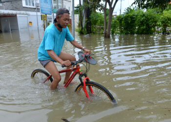 BALI, Seorang pria mengendarai sepeda melalui jalan yang terendam banjir usai diguyur hujan lebat di Bali pada 6 Desember 2021. (Xinhua/Komang Alfan)