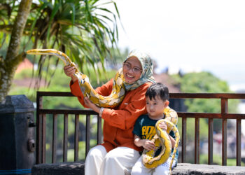 BALI, Dua orang wisatawan berpose untuk difoto di Tanah Lot, Bali, pada 18 Desember 2021. Pulau Bali, destinasi pariwisata yang tersohor di dunia, mencatatkan penurunan jumlah turis internasional yang drastis lantaran pandemi COVID-19. (Xinhua/Xu Qin)