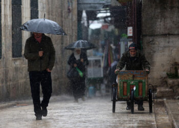 NABLUS, Sejumlah warga Palestina berjalan di sebuah jalan di tengah guyuran hujan di Kota Nablus, Tepi Barat, pada 21 Desember 2021. (Xinhua/Nidal Eshtayeh)