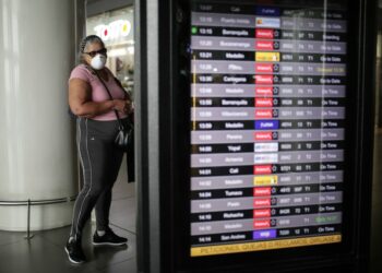 Seorang wanita yang mengenakan masker memeriksa informasi penerbangan di Bandar Udara Internasional El Dorado, di Bogota, Kolombia, pada 16 Maret 2020. (Xinhua/Jhon Paz)