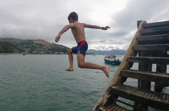AKAROA, Seorang anak laki-laki melompat ke dalam air di sebuah pelabuhan di Akaroa, Selandia Baru, pada 11 Januari 2022. Musim panas biasanya menjadi musim puncak pariwisata di kota tersebut. Namun, tahun ini Akaroa tidak sesibuk biasanya karena dampak COVID-19. (Xinhua/Guo Lei)