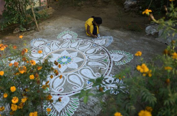 AGARTALA, Seorang anak perempuan melukis "Alpona", atau berbagai motif suci yang berwarna-warni di atas lantai, di halaman di Agartala, ibu kota Negara Bagian Tripura, India timur laut, pada 13 Januari 2022. (Xinhua/Str)
