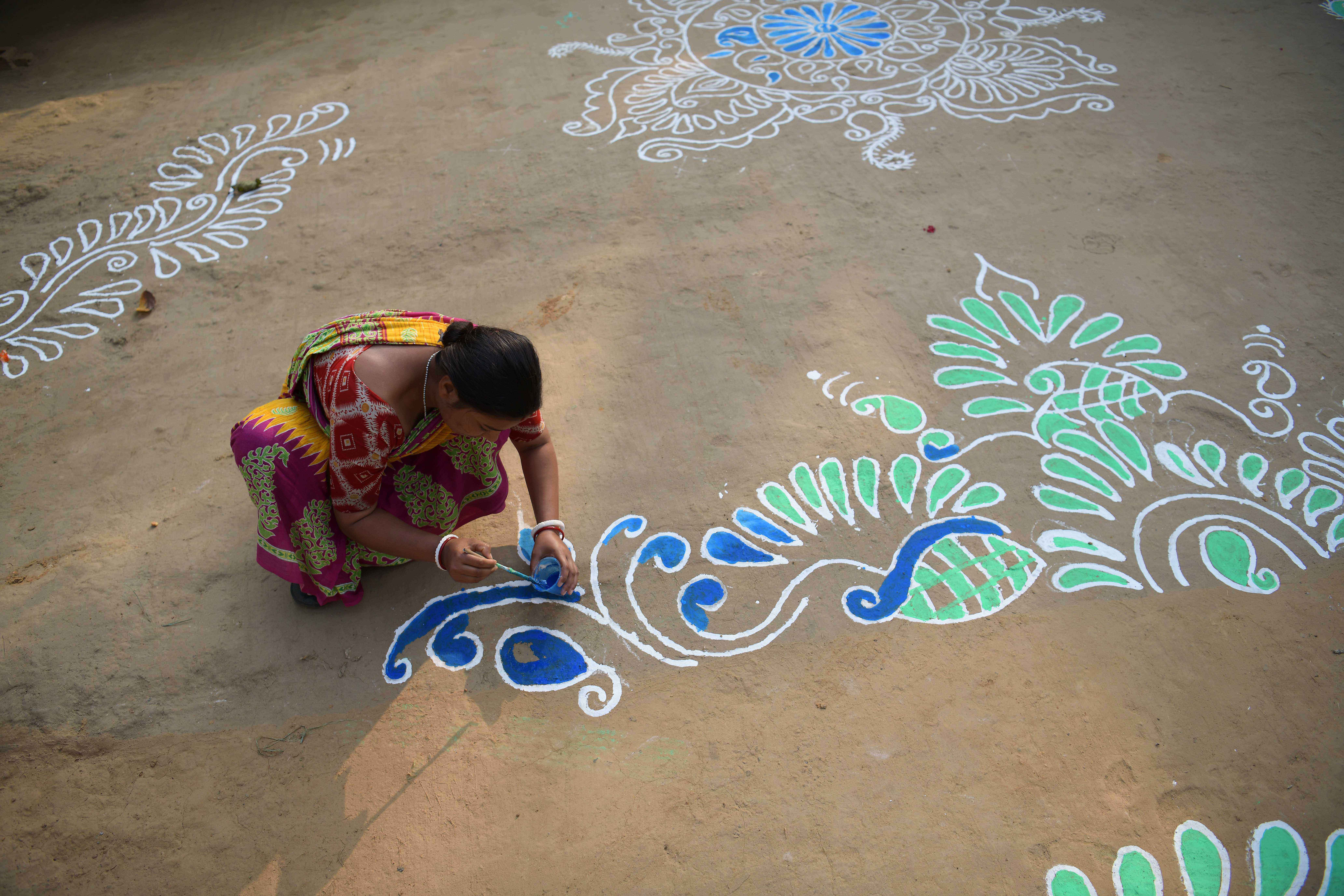 AGARTALA, Seorang wanita melukis "Alpona", atau berbagai motif suci yang berwarna-warni di atas lantai, di halaman di Agartala, ibu kota Negara Bagian Tripura, India timur laut, pada 13 Januari 2022. (Xinhua/Str)