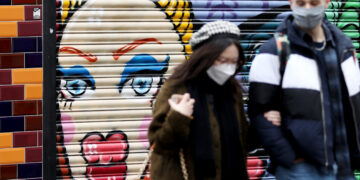 LONDON, Dua orang yang mengenakan masker berjalan melewati grafiti di Brick Lane di London, Inggris, pada 15 Januari 2022. Di London timur, Brick Lane populer dengan seni jalanannya. (Xinhua/Li Ying)