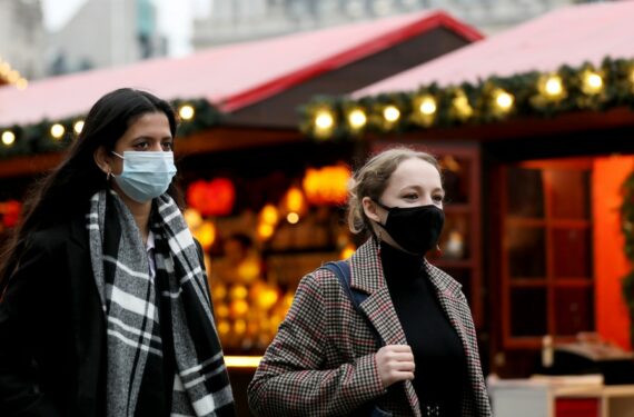 Orang-orang yang mengenakan masker berjalan melewati sebuah stan di pasar Natal yang digelar di Trafalgar Square, London, Inggris, pada 23 Desember 2021. (Xinhua/Li Ying)