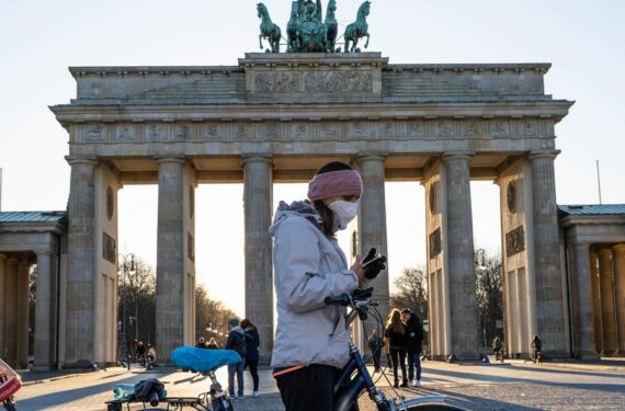 Seorang wanita yang mengenakan masker mengecek ponselnya di depan Gerbang Brandenburg di Berlin, ibu kota Jerman, pada 22 Maret 2020. (Xinhua/Ren Ke)