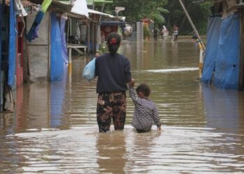 Seorang wanita dan anaknya berjalan menerjang genangan banjir di Desa Sukajaya, Serang, Provinsi Banten, pada 2 Maret 2022. (Xinhua/Shanum Rustika)