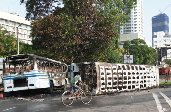 KOLOMBO, Seorang pria berkendara melewati bus-bus yang hancur akibat bentrokan beberapa hari lalu, selagi pelonggaran aturan jam malam selama beberapa jam diberlakukan di Kolombo, Sri Lanka, pada 12 Mei 2022. Sri Lanka memberlakukan jam malam nasional menyusul bentrokan yang diwarnai kekerasan di ibu kotanya, Kolombo, pada 9 Mei. (Xinhua/Tang Lu)