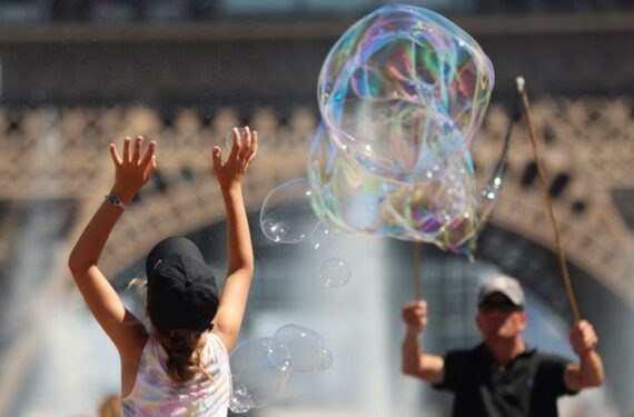 PARIS, Seorang anak perempuan mencoba menangkap gelembung sabun buatan seorang seniman jalanan di dekat Menara Eiffel di Paris, Prancis, pada 16 Juni 2022. (Xinhua/Gao Jing)