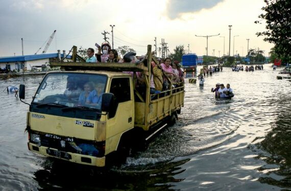 SEMARANG, Orang-orang naik truk bak terbuka mengarungi genangan banjir yang dipicu oleh tingginya air pasang laut di Pelabuhan Tanjung Emas di pesisir Semarang, Provinsi Jawa Tengah, pada 20 Juni 2022. (Xinhua/Rahman Indra)