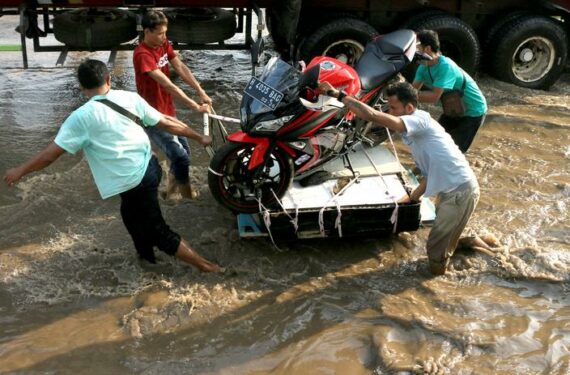 SEMARANG, Sejumlah orang mengangkut sebuah sepeda motor melintasi banjir akibat air pasang di Pelabuhan Tanjung Emas di pesisir Semarang, Provinsi Jawa Tengah, pada 21 Juni 2022. (Xinhua/Rahman Indra)