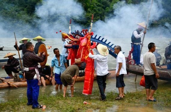 TAIJIANG, Orang-orang dari kelompok etnis Miao menggantungkan kain sutra merah pada sebuah kapal dalam festival perahu naga kano di Shidong di wilayah Taijiang, Provinsi Guizhou, China barat daya, pada 23 Juni 2022. Festival perahu naga kano tahunan kelompok etnis Miao diadakan di Taijiang pada Kamis (23/6). (Xinhua/Yang Wenbin)