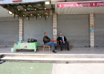 NABLUS, Sejumlah pria Palestina duduk di depan toko-toko yang tutup di sepanjang jalan kosong di Kota Huwara, sebelah selatan Kota Nablus, Tepi Barat, pada 26 Maret 2023. (Xinhua/Nidal Eshtayeh)